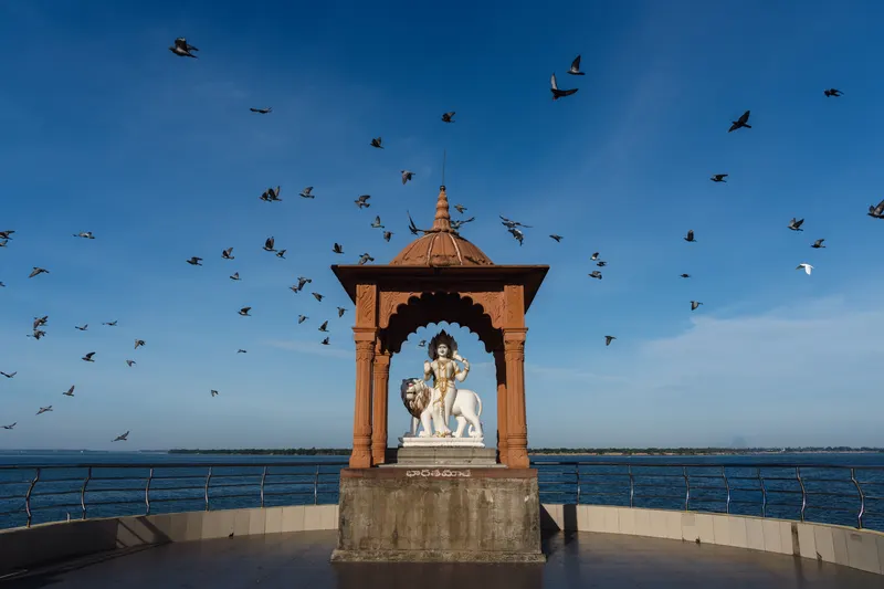 Pigeons wheeling around the Bharata Mata pavilion on the riverfront under a blue sky