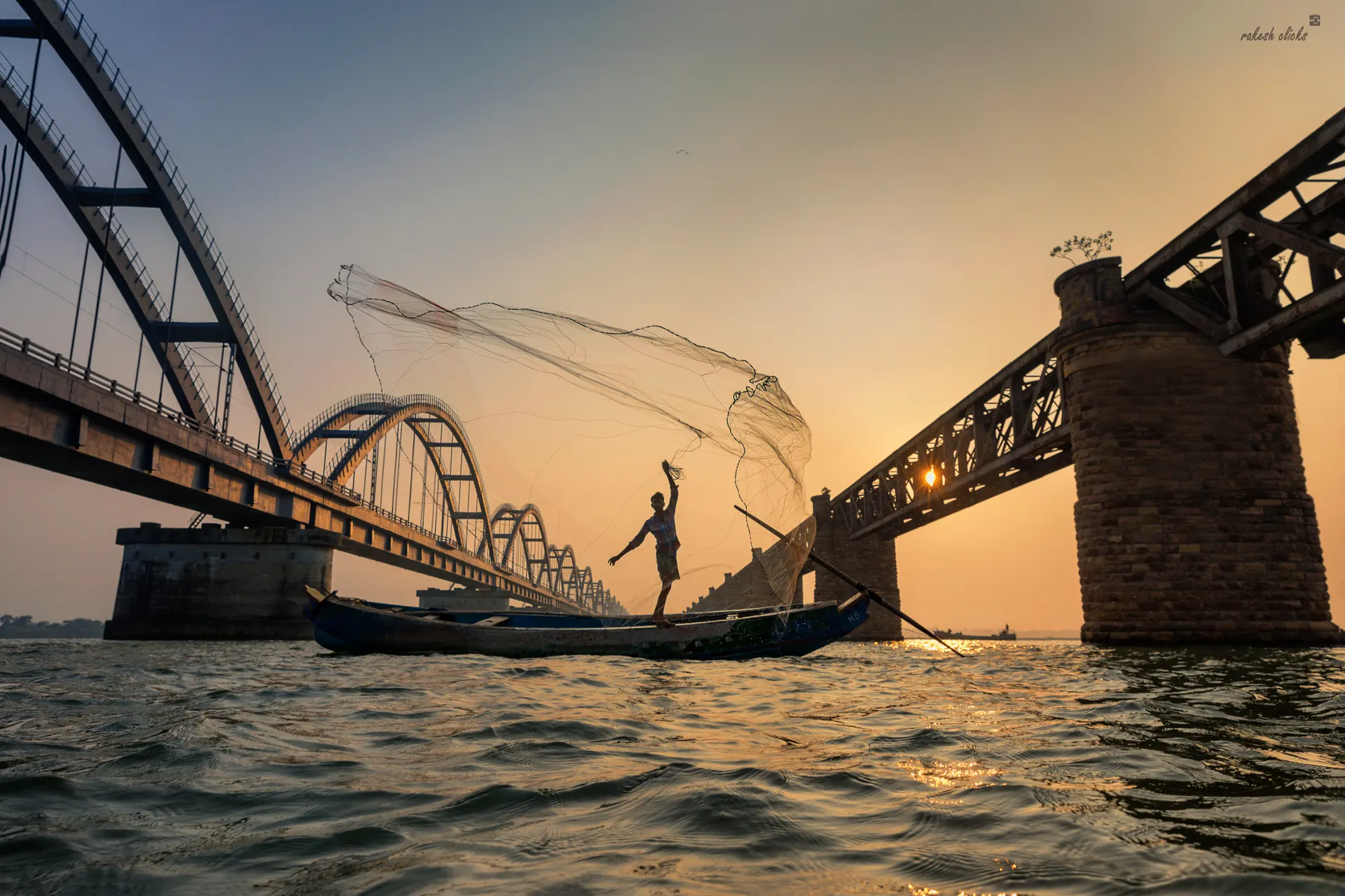 A fisherman casting his net with the Godavari bridges behind
