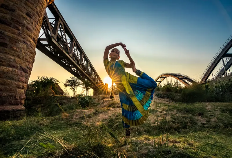 A classical dancer mid-pose at sunset beneath the old rail bridge
