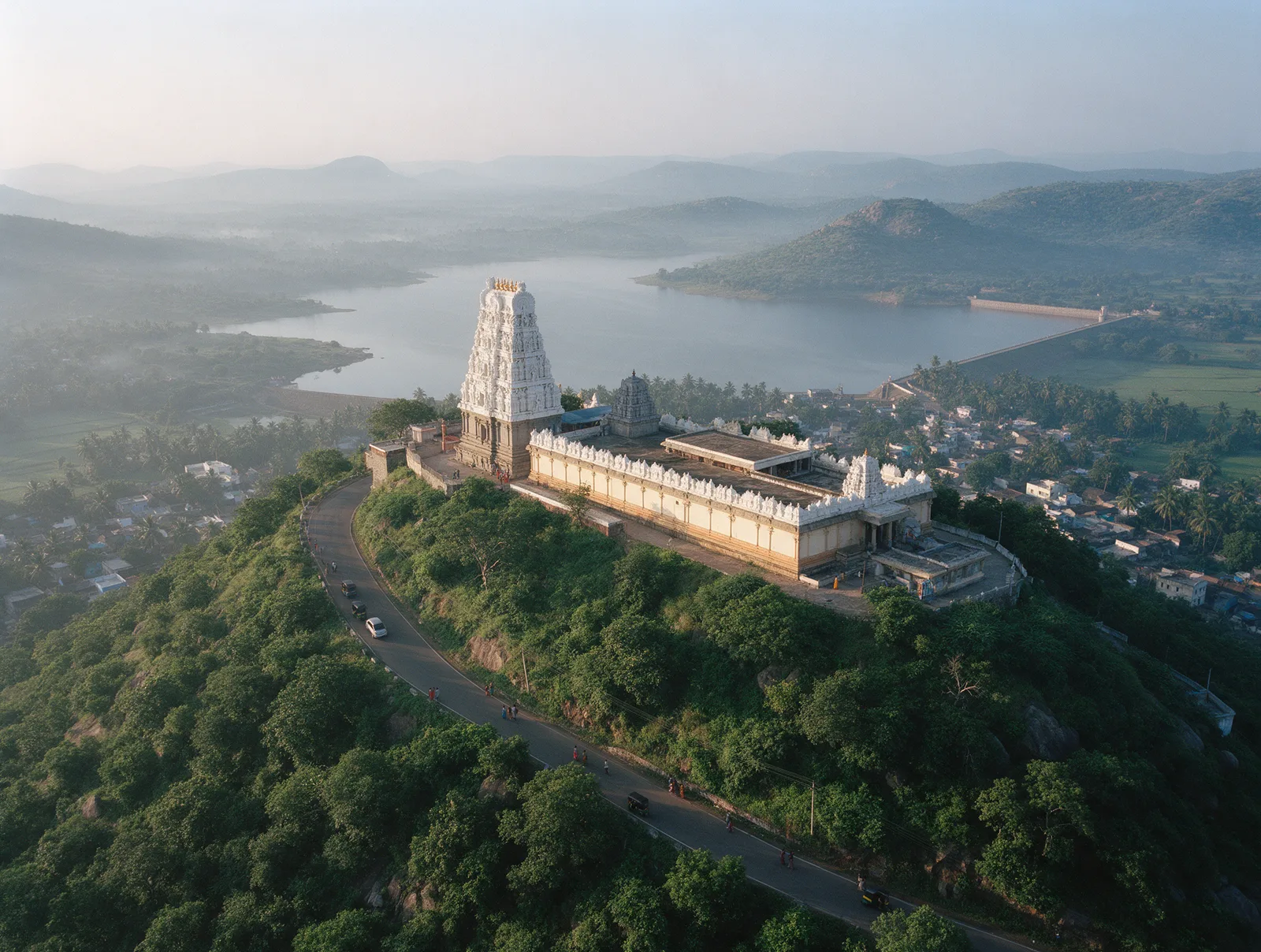 Ratnagiri hill at Annavaram from the air at dawn, the white gopuram of the Satyanarayana temple on the crest and the Pampa reservoir and paddy fields below.