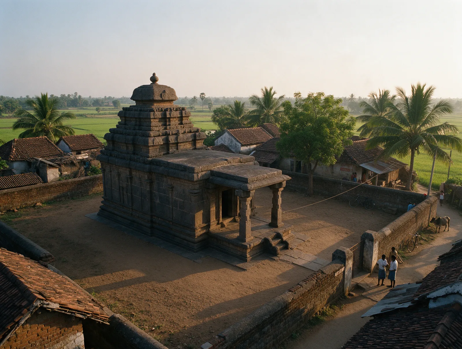 The ninth-century Golingeswara temple at Biccavolu inside its walled village compound, with lanes, tiled houses and trees close around it, seen from the air in golden light.