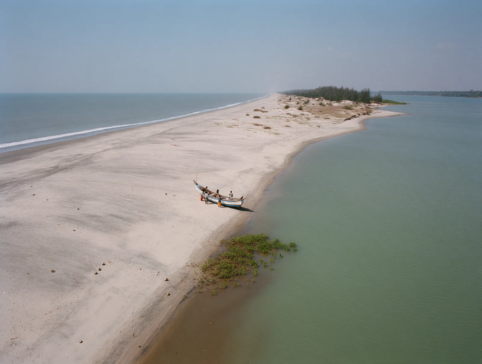 Hope Island from the air, a thin bar of pale sand between the calm bay and the open sea, one fishing boat drawn up on the shore