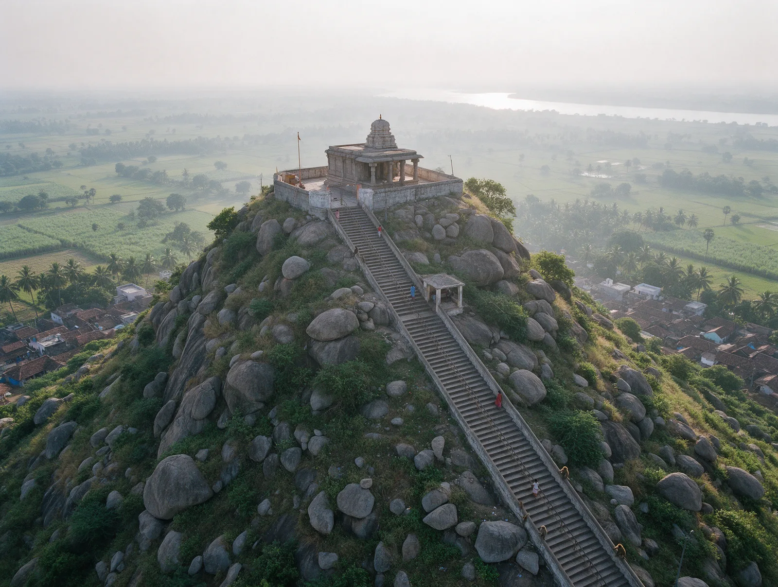 The long stone stairway climbing Korukonda hill to the small Narasimha shrine at the summit, with green delta fields stretching away below.