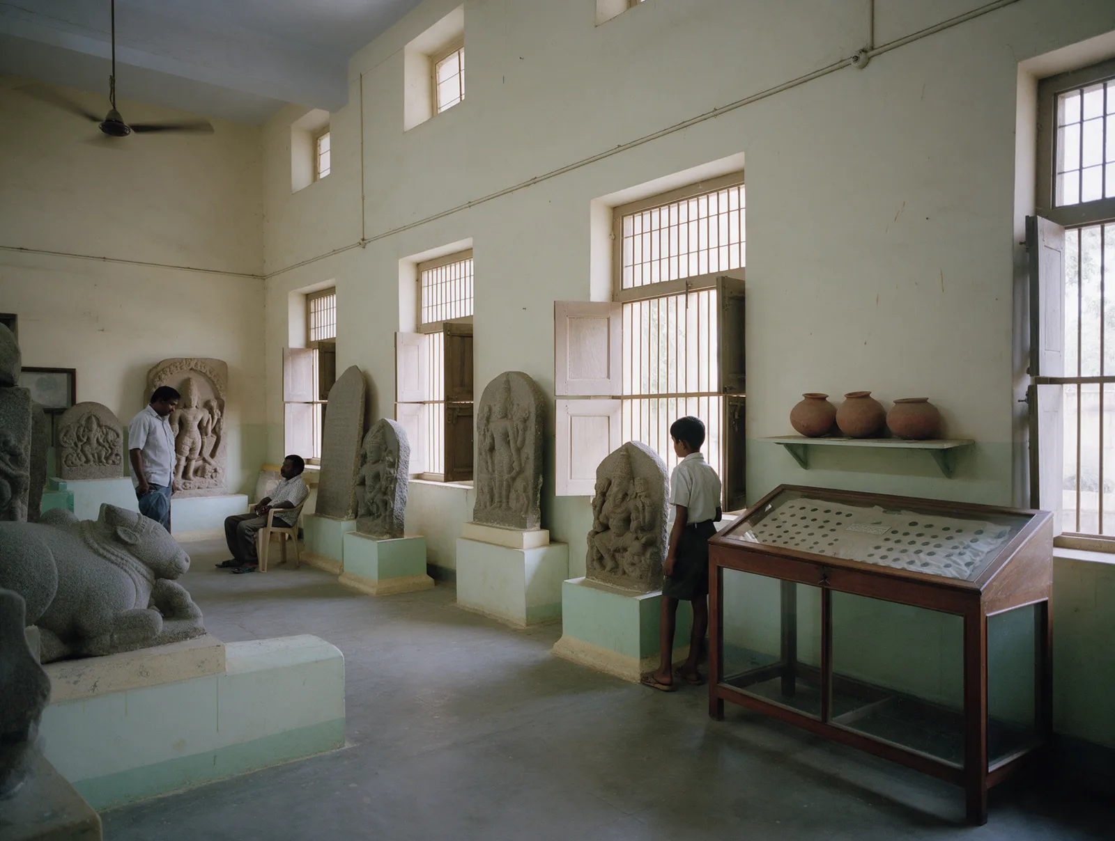 A quiet sculpture gallery in Rajamahendravaram’s government museum, Chalukya stone carvings on plinths under tall daylit windows.