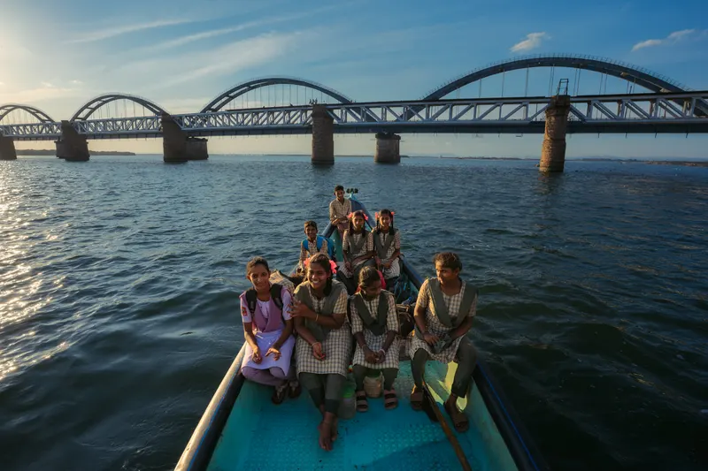 Schoolchildren in uniform riding a country boat, the arched rail bridge behind them