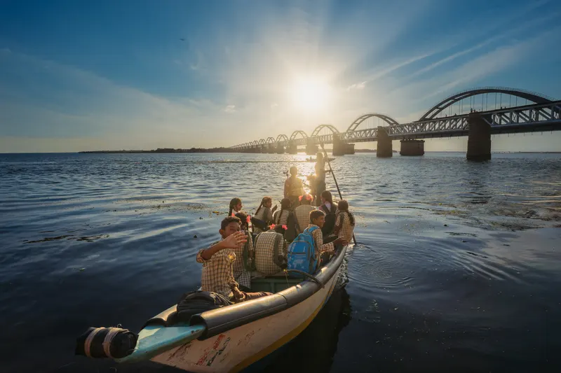 A boat full of schoolchildren waving, heading home towards the bridge at golden hour